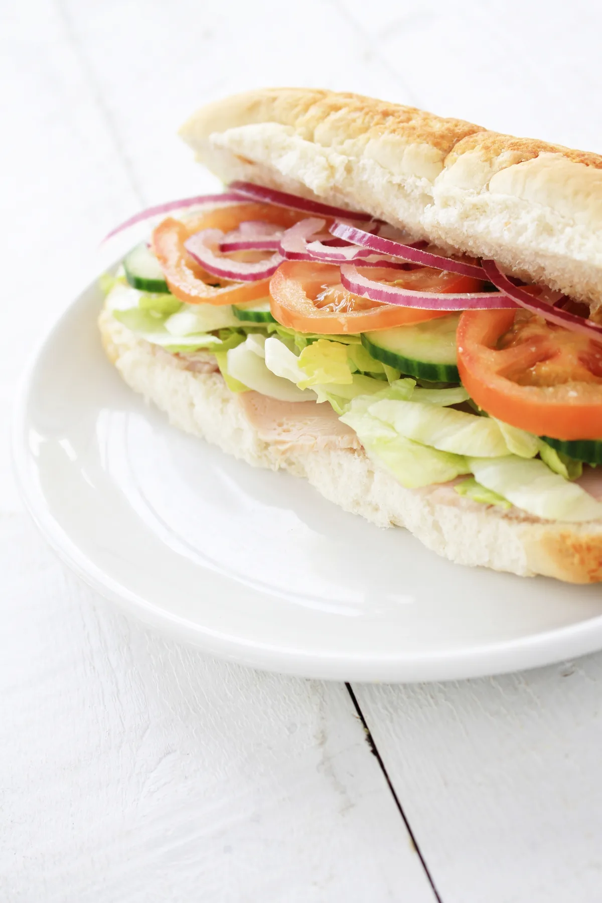Sandwich baguette garni de concombre, tomate, oignon rouge et salade