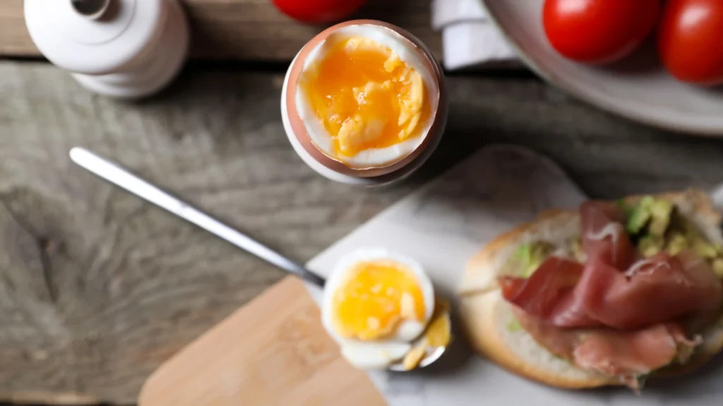 Œuf mollet décalotté dans un coquetier, jaune orange et coulant, avec une tartine au jambon cru
