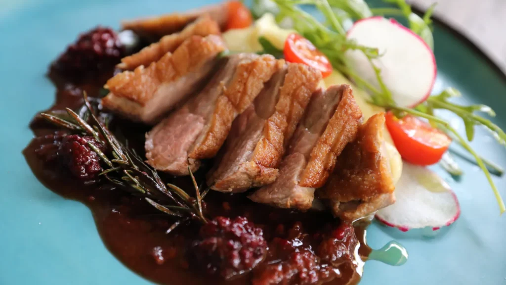 Tranches de magret de canard rosé à la peau dorée et quadrillée, servies avec une sauce aux fruits rouges et du romarin